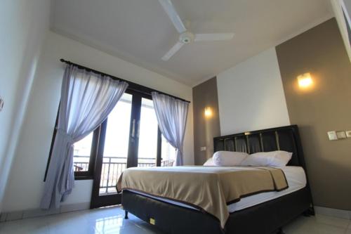 a bedroom with a bed and a large window at De Dukuh Guest House in Kuta