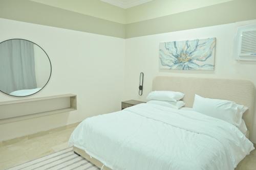 a white bedroom with a bed and a mirror at Modern & New furnished Apartments - 10 Mins Drive to Beach in Al Bādīyah