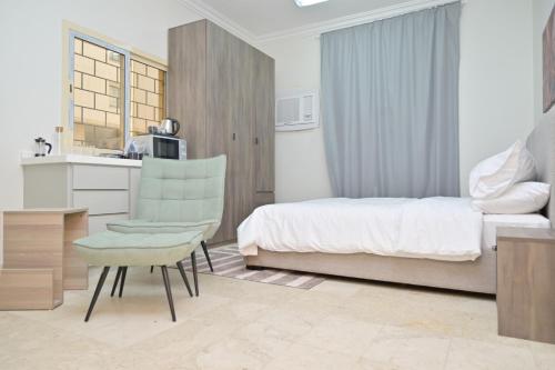 a bedroom with a bed and a chair and a kitchen at Modern & New furnished Apartments - 10 Mins Drive to Beach in Al Bādīyah