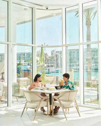 two people sitting at a table in a room with windows at Vida Marina marassi hotel apartment with extra fees for beach or pool access شقة فندقية عائلات فقط في أوتيل فيدا مراسي مارينا دخول شاطئ البحر او حمام السباحة برسوم إضافية in El Alamein