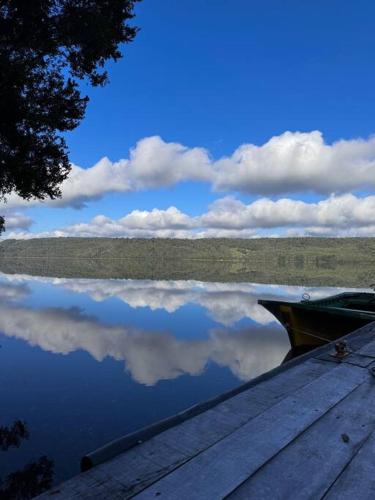 a boat sitting on a lake with its reflection in the water at Refugio Mayapehue, Lago Natri Chiloé in El Púlpito
