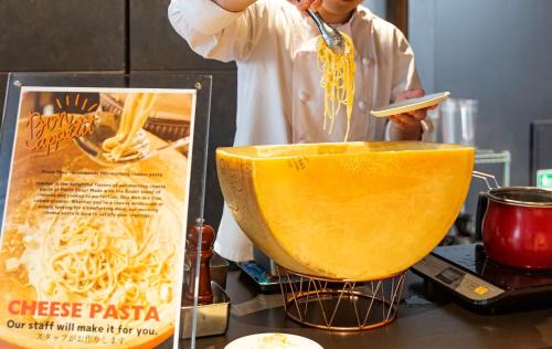 a man is mixing spaghetti in a bowl at Hotel Keihan Namba Grande in Osaka