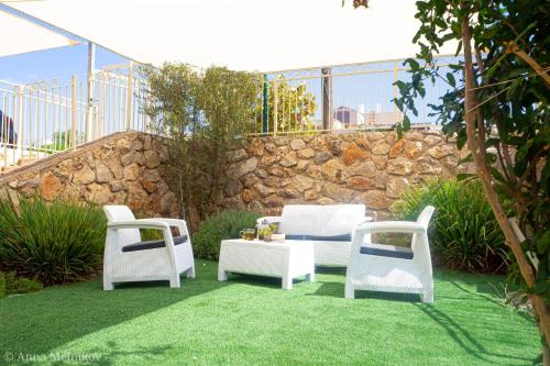 three white chairs and a table and a stone wall at יפעת הגלבוע -סוויטות אירוח ברמה אחרת in Nurit