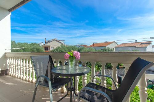 a table and chairs on a balcony with a vase of flowers at Apartment Damir in Brodarica
