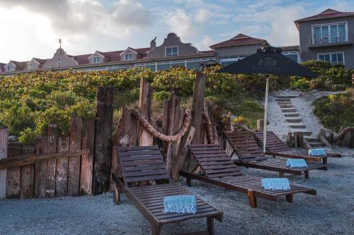 a row of beach chairs with an umbrella and a fence at Blue Bay Lodge in Saldanha
