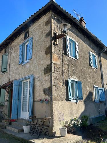 a house with blue shutters and a table in front of it at La petite maison d'Arbas in Arbas