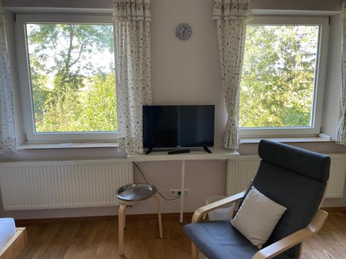 a living room with a chair and a tv and two windows at Ferienwohnungen Ollarzried in Ollarzried