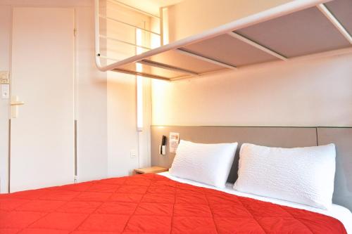una camera da letto con un letto con lenzuola rosse e cuscini bianchi di Premiere Classe Saint Nazaire - Trignac a Trignac