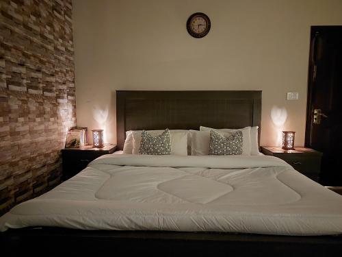 a large white bed with pillows and a clock on the wall at Green Residency, Eco-Friendly Guestrooms available for Families near Islamabad and Murree in Islamabad