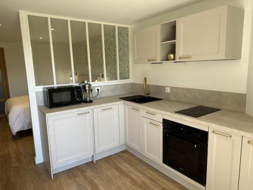 une cuisine avec des armoires blanches et un appareil noir dans l'établissement Manoir de l Aiguillon, à Ranville