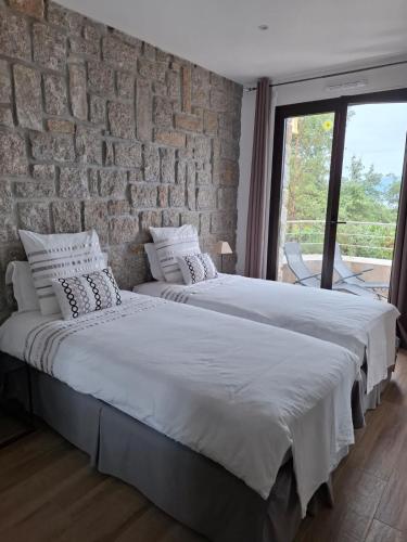 - 2 lits dans une chambre avec un mur en briques dans l'établissement Camélia Plein Soleil Bord de Plage, à Coti-Chiavari