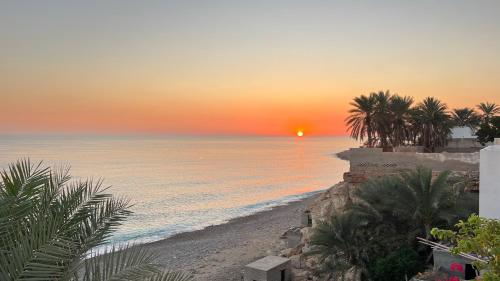 a sunset over a beach with palm trees and the ocean at Wadi shab Beach Resort in Sur