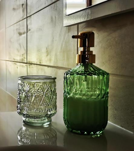 - une bouteille de savon vert à côté d'une tasse de verre dans l'établissement Chez Aurel & Manu, à Sainte-Marie-aux-Mines
