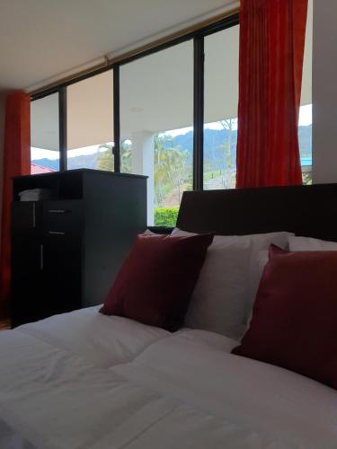 a bed with red pillows in a room with windows at Hotel & restaurante campestre la siria in San Juan de Rioseco 