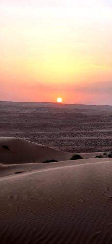 a sunset in the desert with the sun in the horizon at Starry Domes Desert Camp in Badīyah