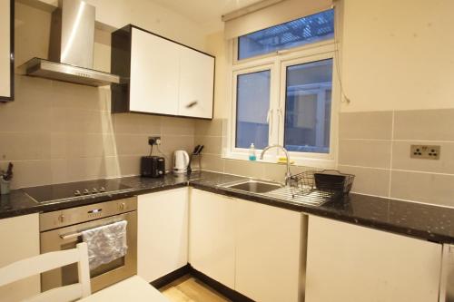 a kitchen with white cabinets and a sink and a window at Evergreen Apartments- Flat 2 in London