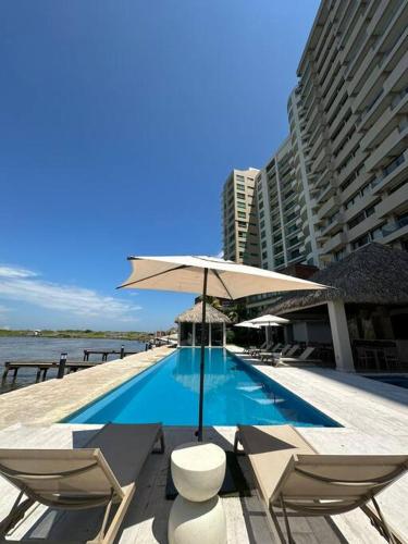 a swimming pool with chairs and an umbrella at Departamento acogedor con vista al mar y alberca in Conchal