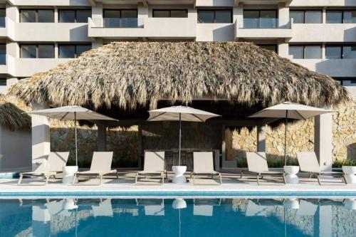 a pool with chairs and umbrellas next to a building at Departamento acogedor con vista al mar y alberca in Conchal