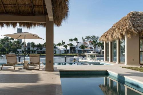 a resort pool with two chairs and an umbrella at Departamento acogedor con vista al mar y alberca in Conchal