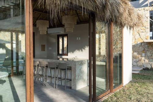 a kitchen with a bar with stools under a straw roof at Departamento acogedor con vista al mar y alberca in Conchal