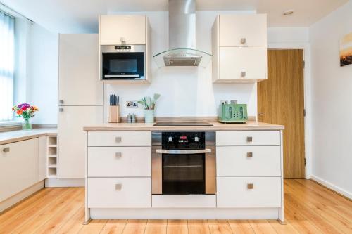 a kitchen with white cabinets and a stove at Spacious 2-Bed Apartment in Liverpool Cavern Quarter - Minutes from Bars and Live Music by Garudy Serviced Apartments in Liverpool