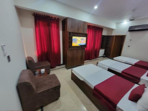 a bedroom with two beds and a chair and a television at Airport Guest House - JIA in Karachi