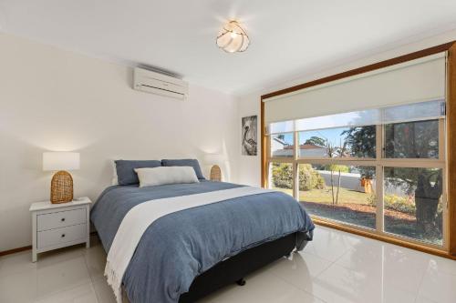 a bedroom with a bed and a large window at Colloden Beach House by Experience Jervis Bay in Vincentia