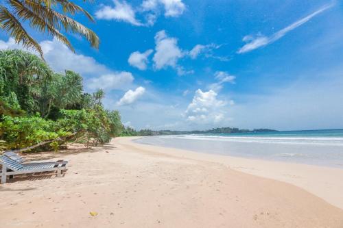 a beach with a bench on the sand and the ocean at Family Villa Talalla in Talalla