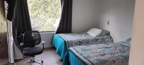 a bedroom with two beds and a chair and a window at Hermosa casa parcela puerto varas in Puerto Varas