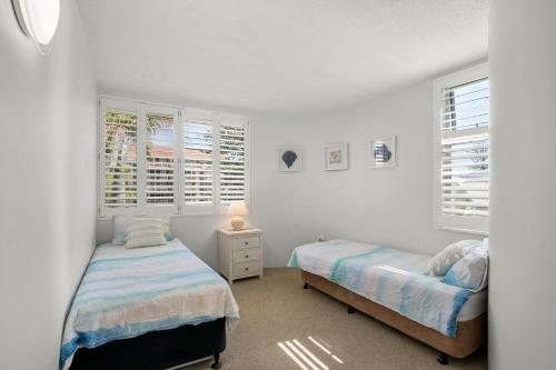 two beds in a bedroom with white walls and windows at Monterey Lodge Unit 17, 27 Warne Tce Kings Beach in Caloundra