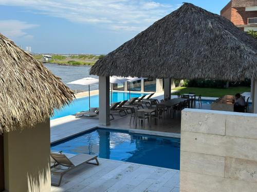 a resort with a swimming pool with chairs and a straw umbrella at Departamento acogedor con vista al mar y alberca in Conchal