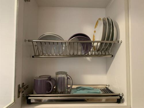 a cupboard with plates and mugs on a shelf at Fancy and Nice 2BR at Tokyo Riverside PIK 2 Apartment By Travelio in Rawalembang