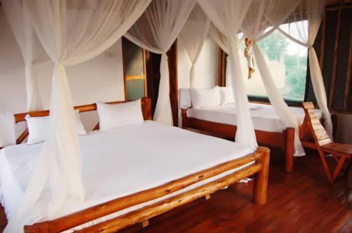 a bedroom with two beds with curtains and a chair at Entale Safari Camp Queen Elizabeth National Park in Kasese