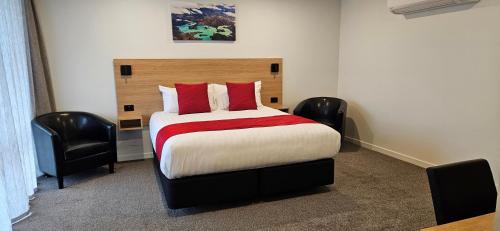 a bedroom with a bed with red pillows and two chairs at Alps Motel & Apartments in Twizel