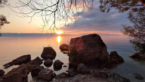 a sunset over the water with rocks in the water at Rooms and Apartaments De Niro in Trpejca