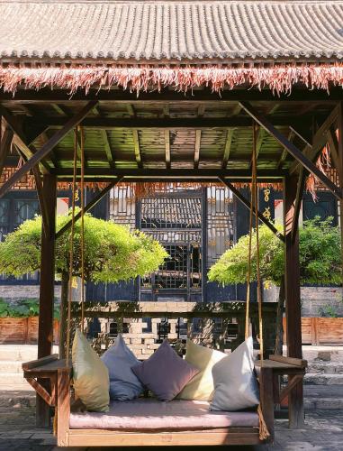 a wooden swing with pillows on it at Elsewhere Hotel The former residence of the draft bank in Pingyao