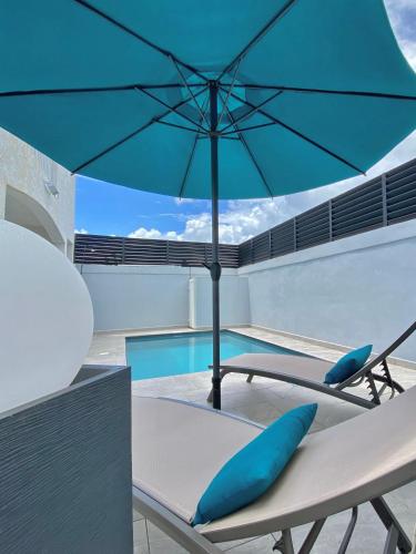 a blue umbrella sitting on a chair next to a pool at Villa - Cosy - Piscine - Guadeloupe centre in Baie-Mahault