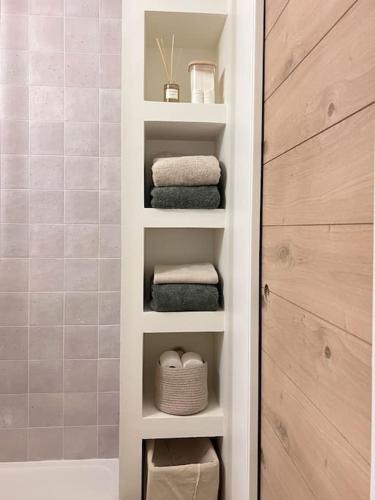 La salle de bains est pourvue d'étagères blanches, de serviettes et d'une douche. dans l'établissement Baby Jane, Studio front de neige, à Isola