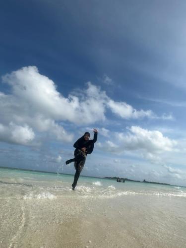 a man is standing in the water on the beach at Chao Guest House in Maafushi