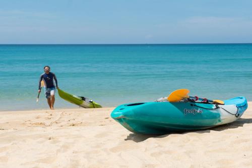 a man walking on the beach with a kayak on the beach at Villa Ananda at Jivana Beach Villas in Pilai Beach