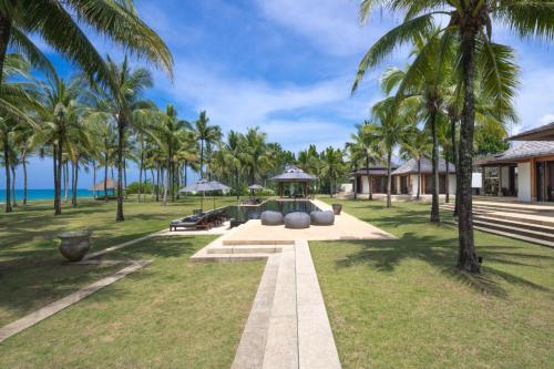 a garden with palm trees in front of a resort at Villa Ananda at Jivana Beach Villas in Pilai Beach