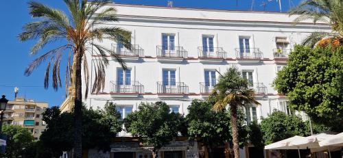 a white building with balconies and palm trees at Apartamentos Arenal in Jerez de la Frontera