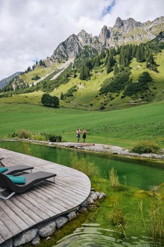 two people standing on a boardwalk next to a river with mountains at Arlberg Stuben - das kleine, feine Hotel in Stuben am Arlberg