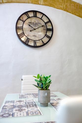 a clock on a wall above a table with a plant at Authentic Townhouse with backyard in Sliema by 360 Estates in Sliema