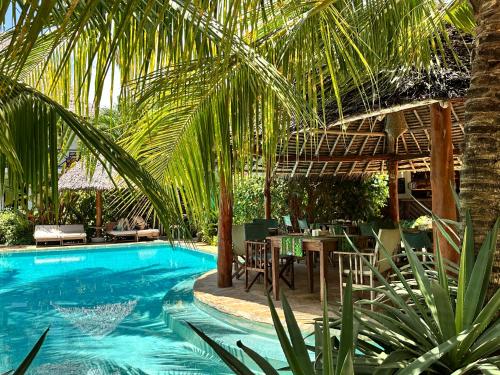a pool with tables and chairs and a palm tree at Maisha Nungwi - Boutique Hotel in Nungwi