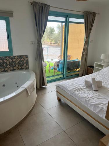 a bathroom with a tub and a bed and a window at בקתה במטע מושב אליעד in Eli Ad