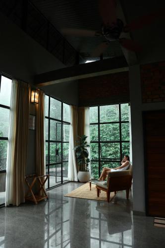 a woman sitting in a chair in a room with windows at Bhadra - The Estate Villa in Wayanad