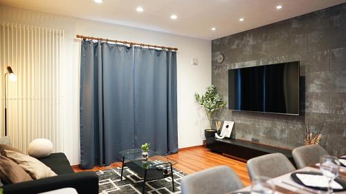 a living room with a couch and a tv on a wall at HOTELHOUSE Nekogoya Hachiken 八軒 in Ōdōri