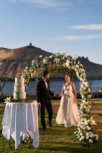 a bride and groom walking under an arch with a wedding cake at Mövenpick Resort Aswan in Aswan