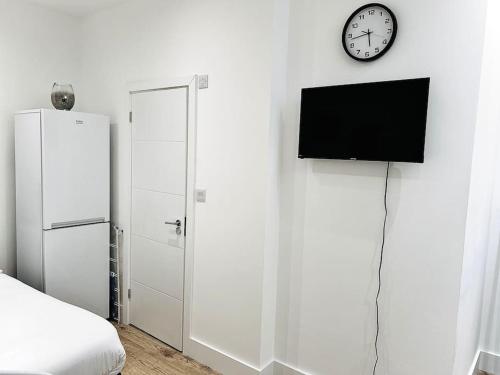 a bedroom with a white wall with a clock and a tv at Cozy Fully Equipped Loft Studio City Centre in Maidstone